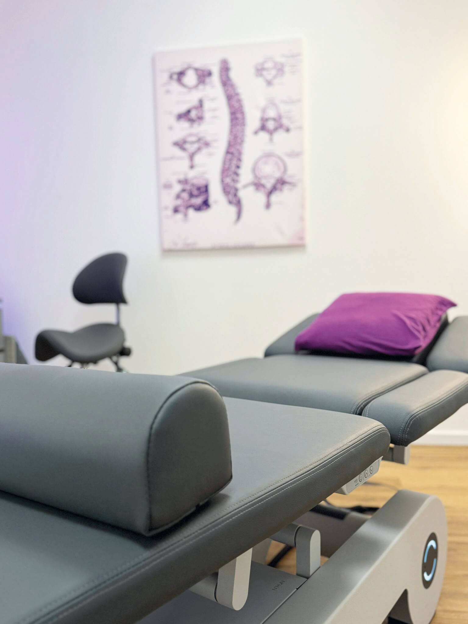 Behandlungsraum der Gesundheitszentrale Amelsbüren mit Therapieliege, Sattelhocker und Wirbelsäulen-Poster an der Wand